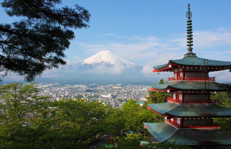In primo piano una pagoda giapponese e sullo sfondo il monte Fuji innevato con sotto una città giapponese