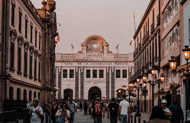 Strada affollata di Lima con tanti passanti in primo piano e in fondo un istituto letterario del Perù