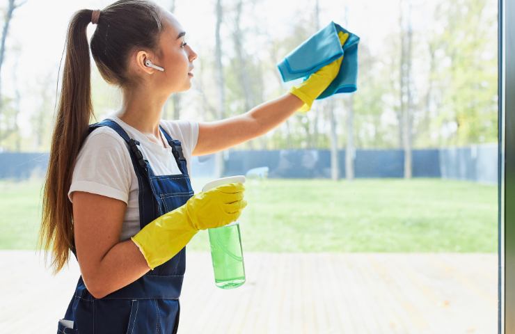 Una ragazza che pulisce i vetri con spruzzino e panno